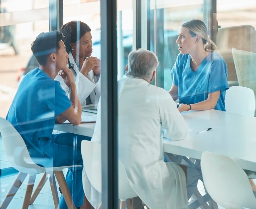 A group of doctors in a conference room, sitting at a table talking.