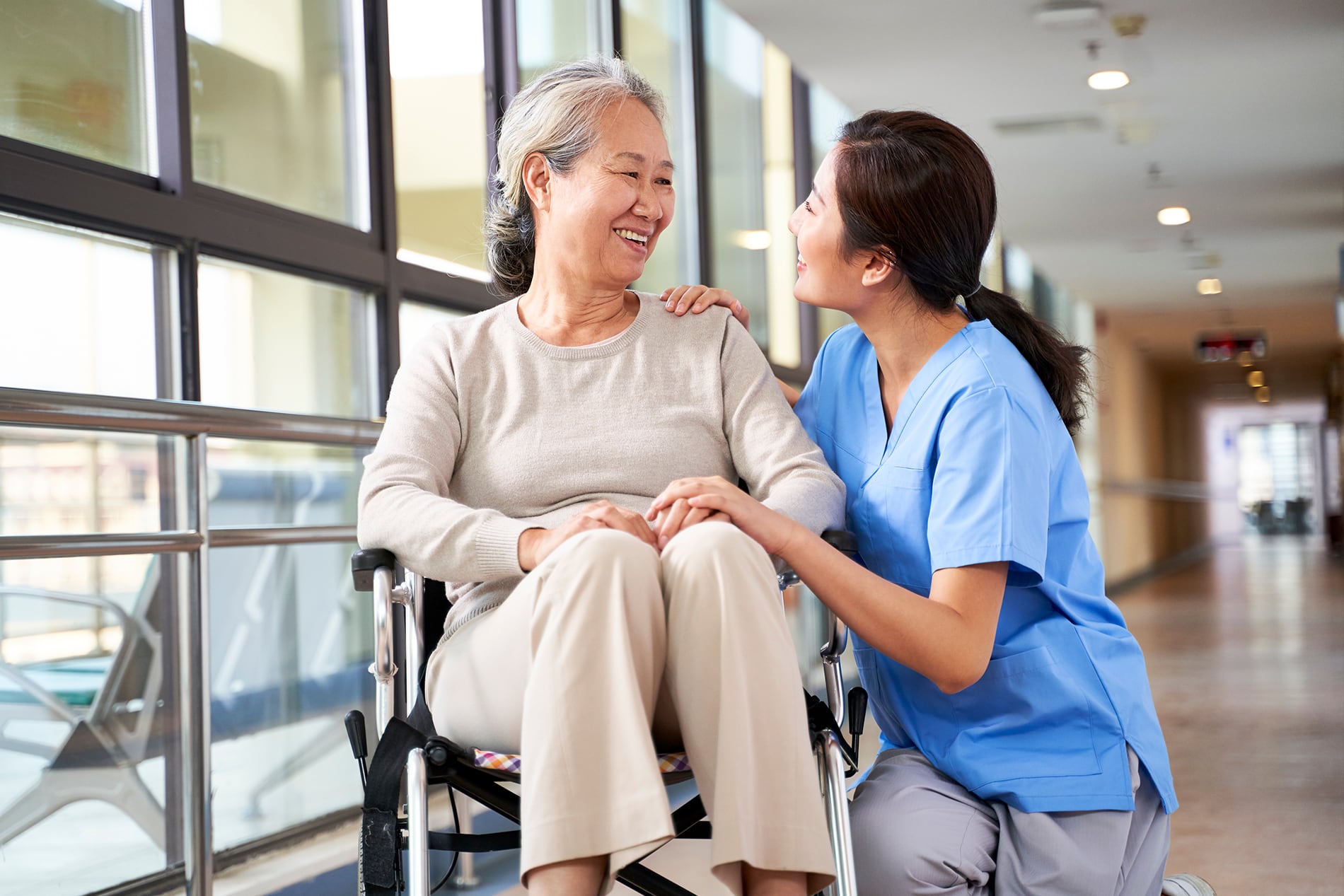 UDS-resource-section A woman nurse kneeling down next to an elderly woman in a wheelchair, talking together.